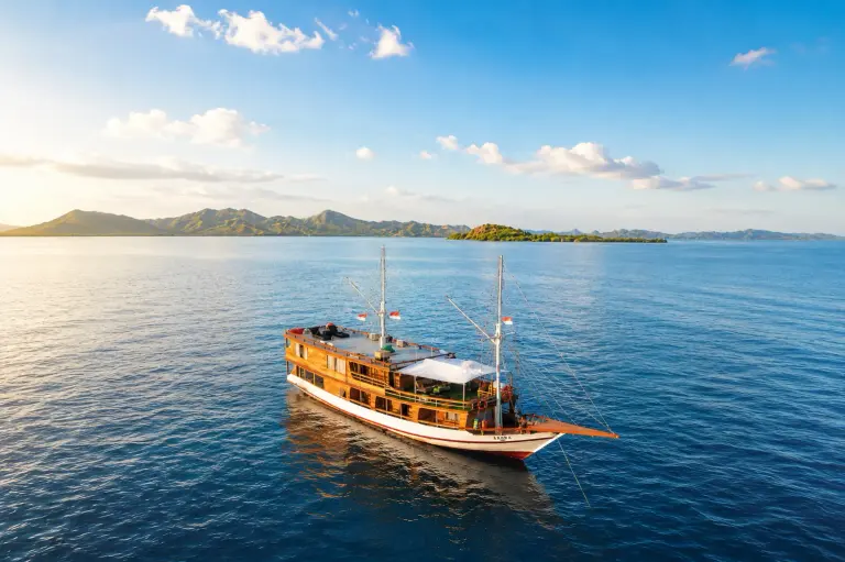 The Arora phinisi sailing in Komodo waters with hills in the distance