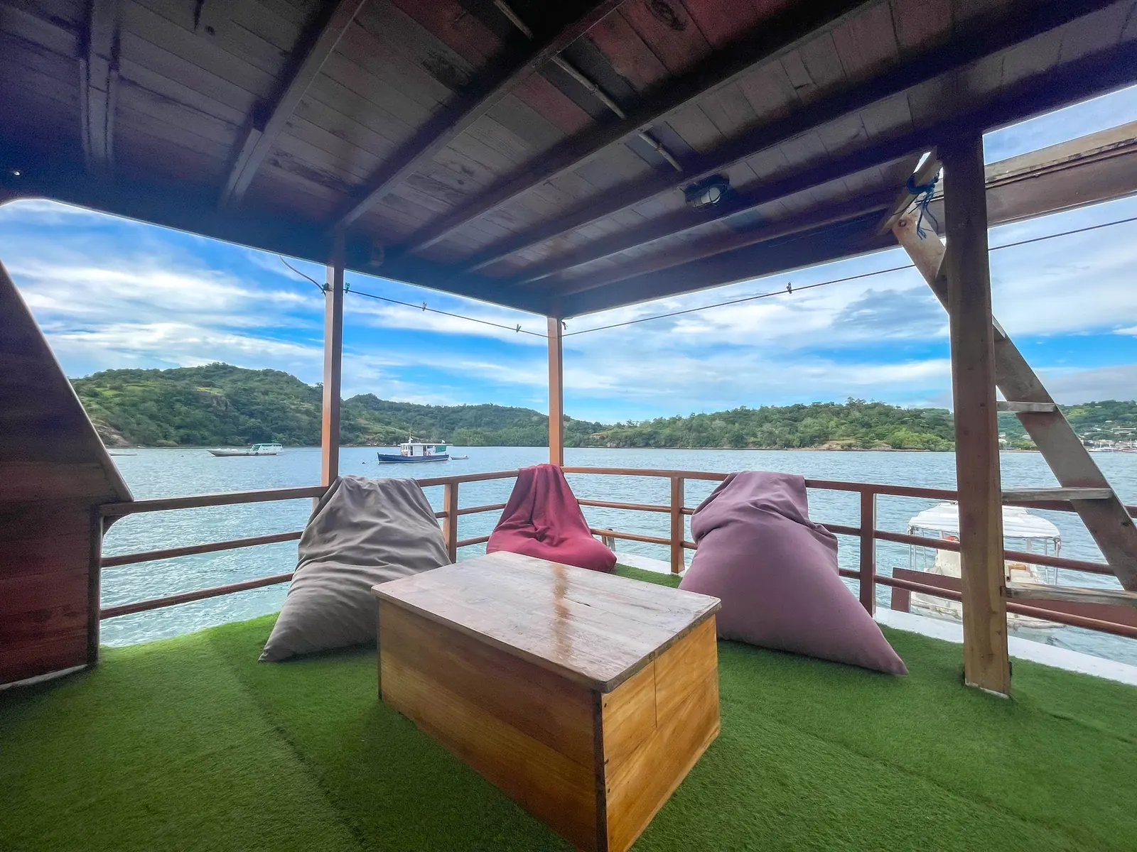 Area santai berlantai rumput sintetis dengan bean bag menghadap laut
