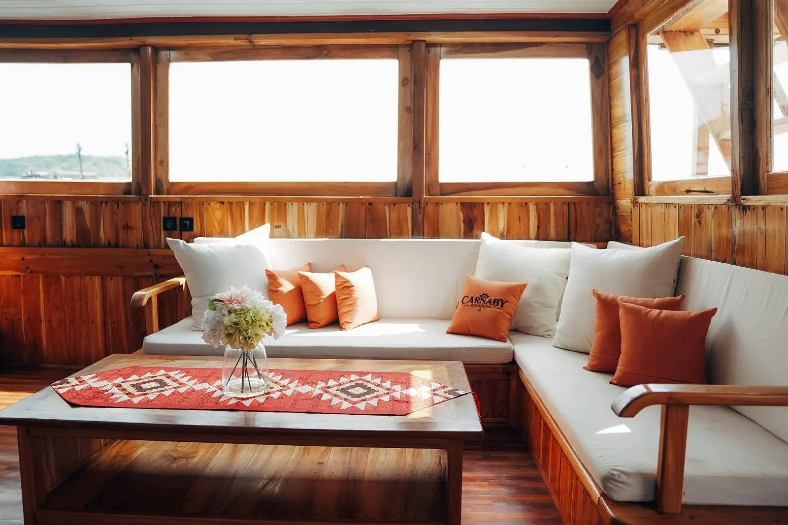 Lounge dalam Carnaby II, sofa putih berbantal oranye mengelilingi meja kayu