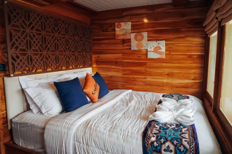 Suite Cabin dek utama Carnaby II, ranjang double dengan bantal oranye dan dinding kayu