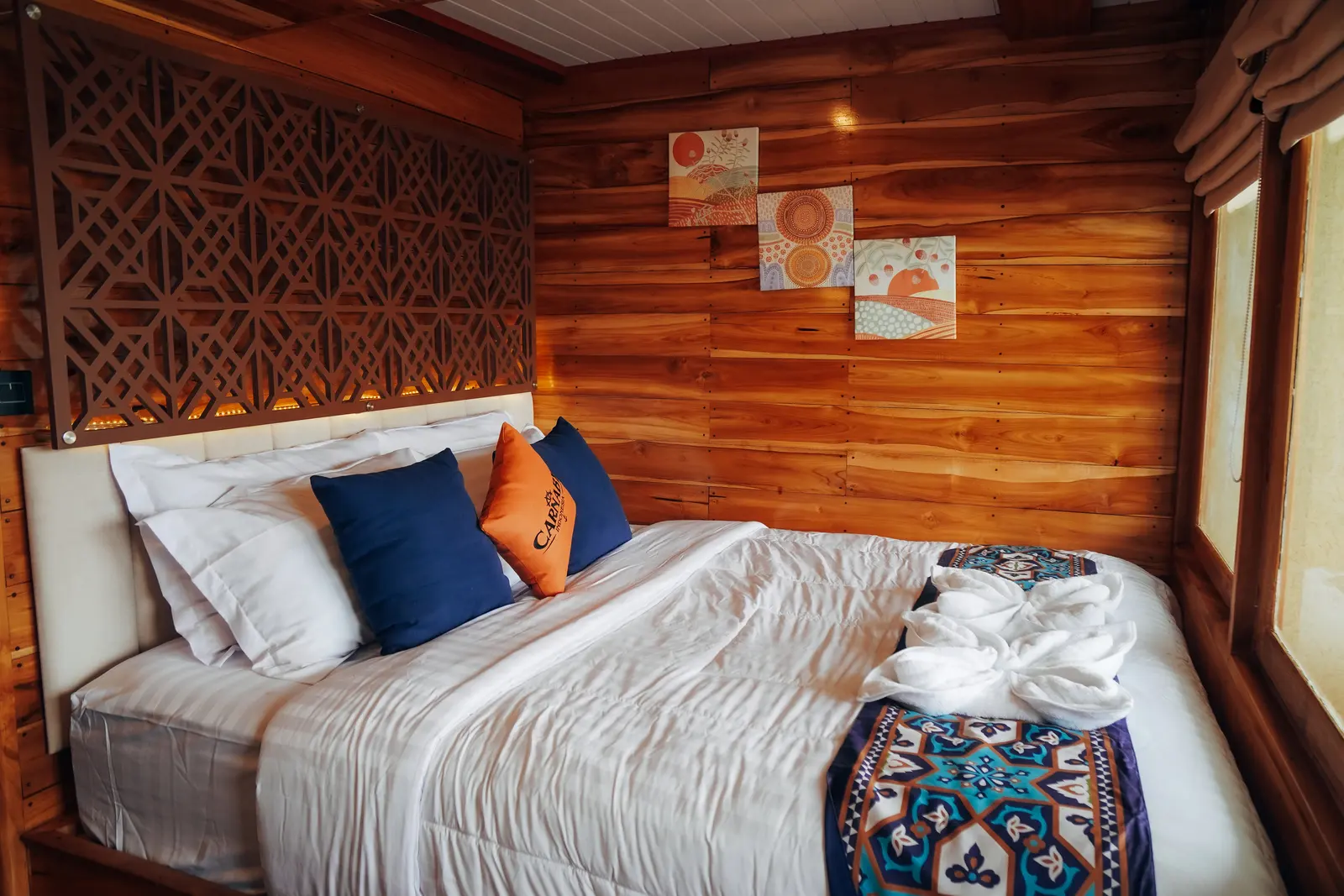 Suite Cabin dek utama Carnaby II, ranjang double dengan bantal oranye dan dinding kayu