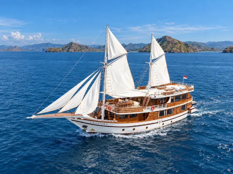 Cassandra, phinisi kayu dengan layar putih penuh di laut biru di perairan Taman Nasional Komodo