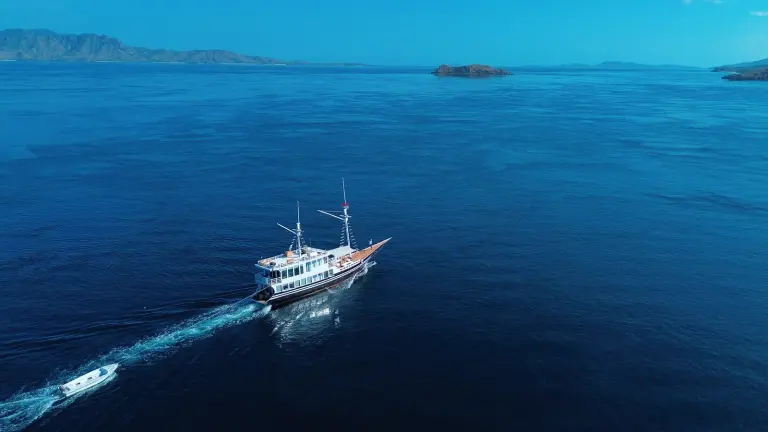 Dark-hulled Derya phinisi sailing the blue water of Komodo National Park, towing its dinghy