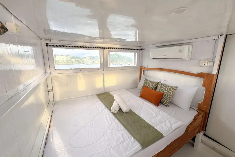 Kabin Deluxe dek atas Diara La Oceano, kasur queen dengan bantal hijau dan jendela ke arah pelabuhan