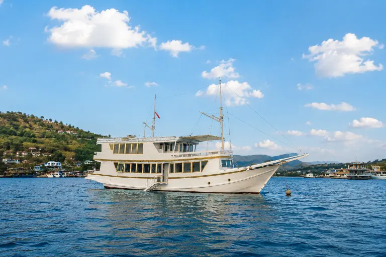 The white-hulled Elyona phinisi at anchor in a blue Labuan Bajo bay