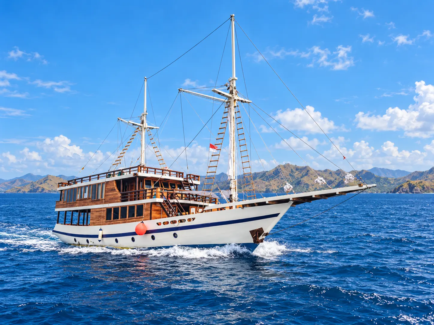 Kanthaka, a two-masted wooden phinisi under way with spray at the bow in Komodo National Park waters