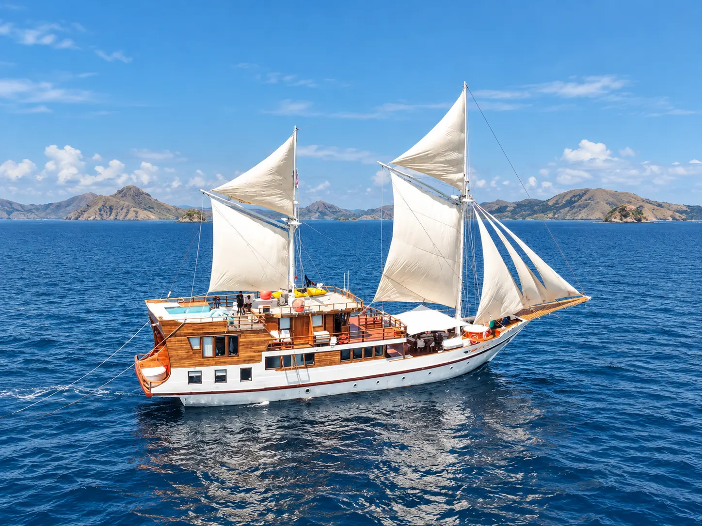 Lady Grace, a wooden phinisi with white sails up on blue water in Komodo National Park waters