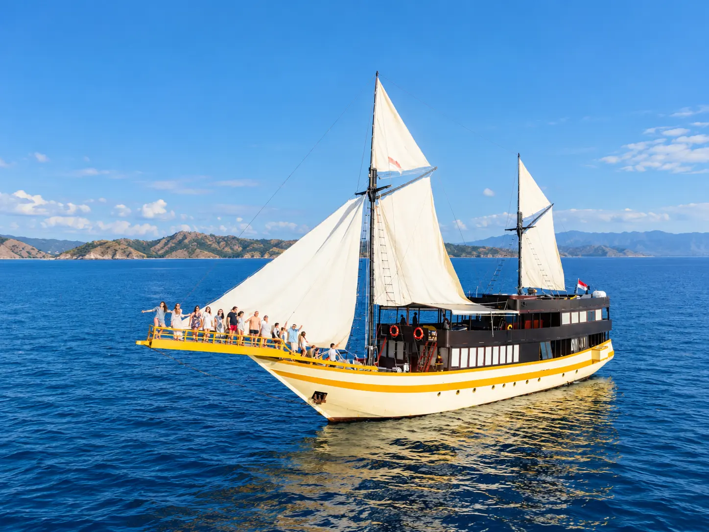 Lamborajo 3, a yellow-hulled phinisi with white sails in Komodo National Park waters