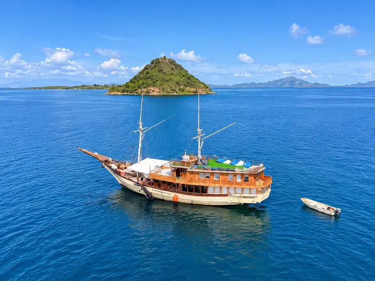 Leticia Liveaboard, phinisi kayu berlabuh dekat pulau hijau di perairan Taman Nasional Komodo