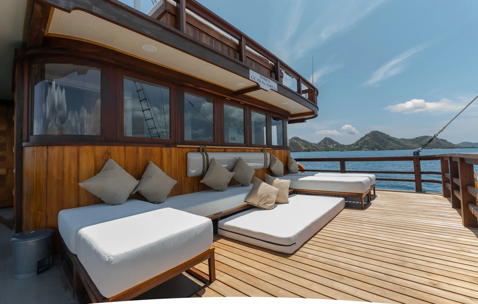 Dek lounge Marea dengan sofa dan daybed berbantal di bawah atap