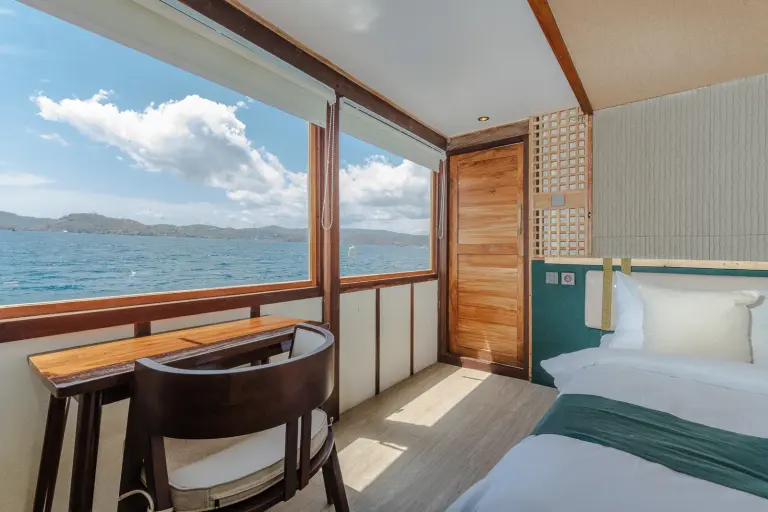 Deluxe Cabin Marea, jendela lebar ke laut dengan meja dan kursi kayu di depannya