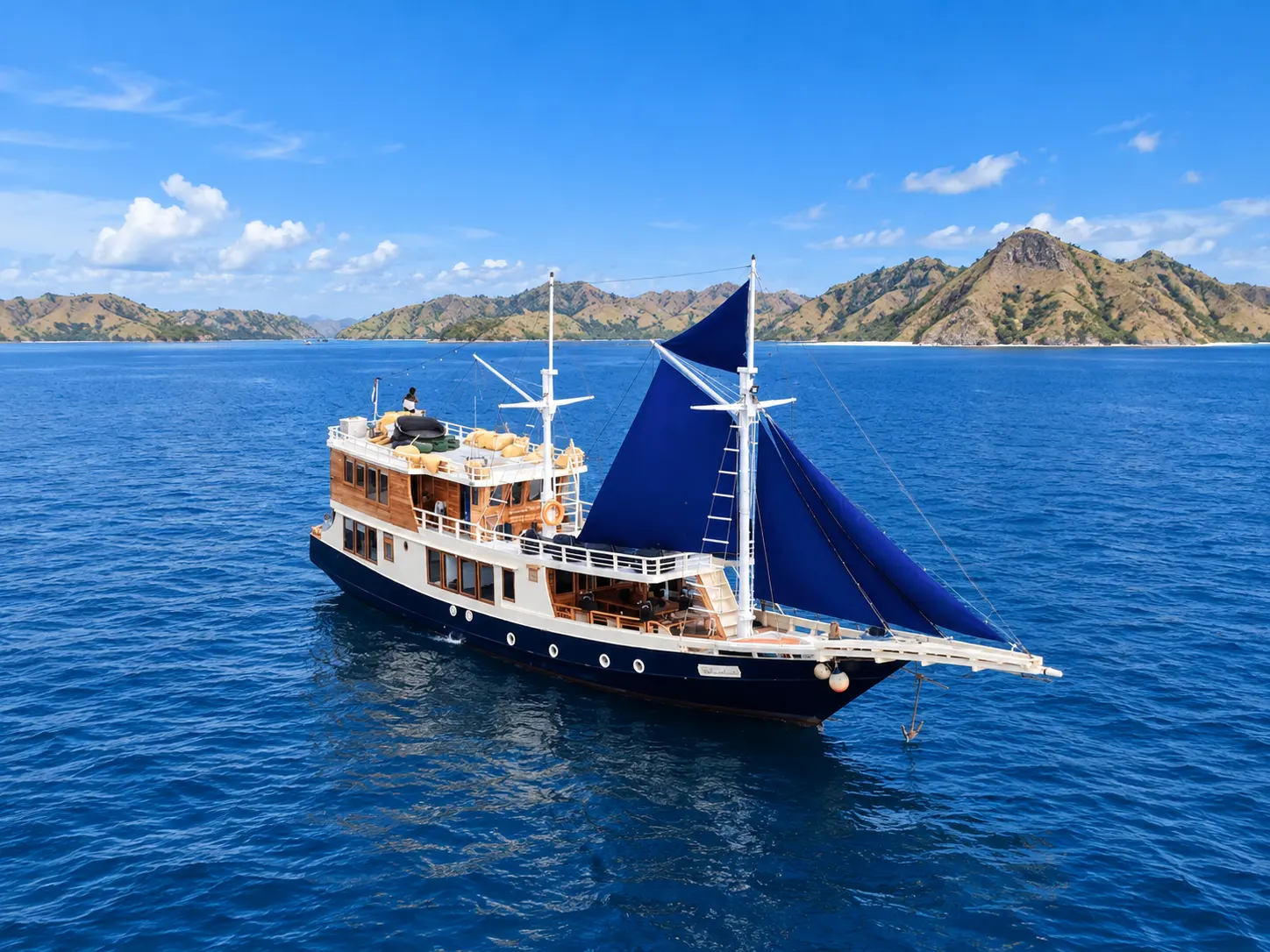 Natural, a black-hulled phinisi with a blue sail in Komodo National Park waters