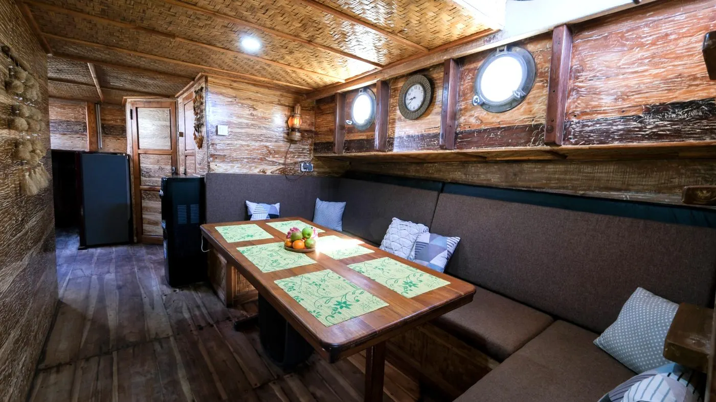 Ruang makan dalam Sabbar Cruise, meja kayu tertata dan sofa berbantal di sepanjang dinding