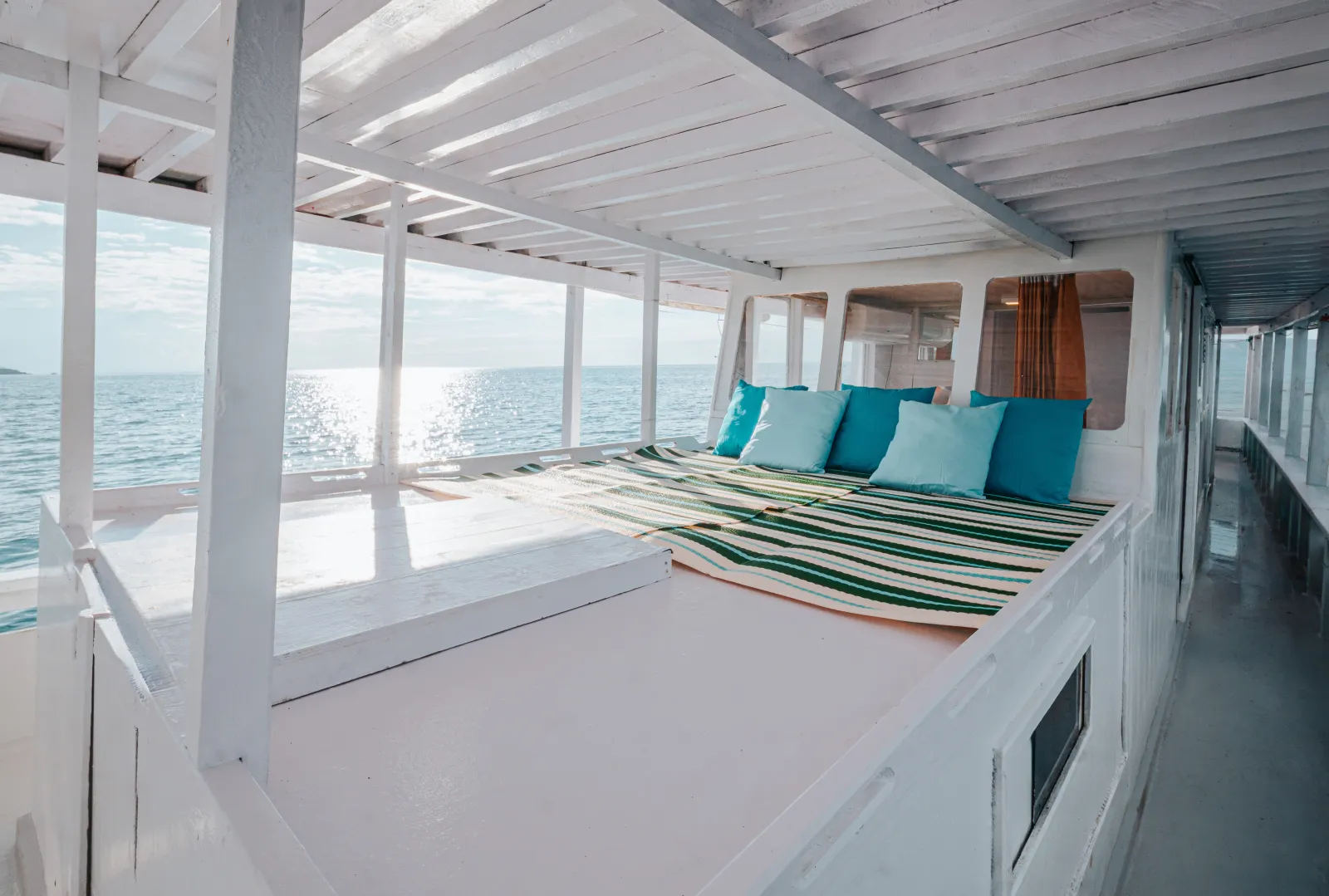 Lounge dek Sabira, daybed bergaris dengan bantal toska menghadap laut