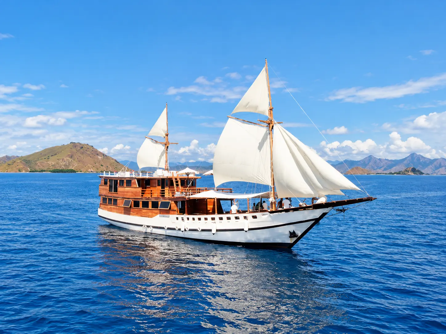 Vinca, phinisi kayu dengan layar putih dekat pulau cokelat di perairan Taman Nasional Komodo